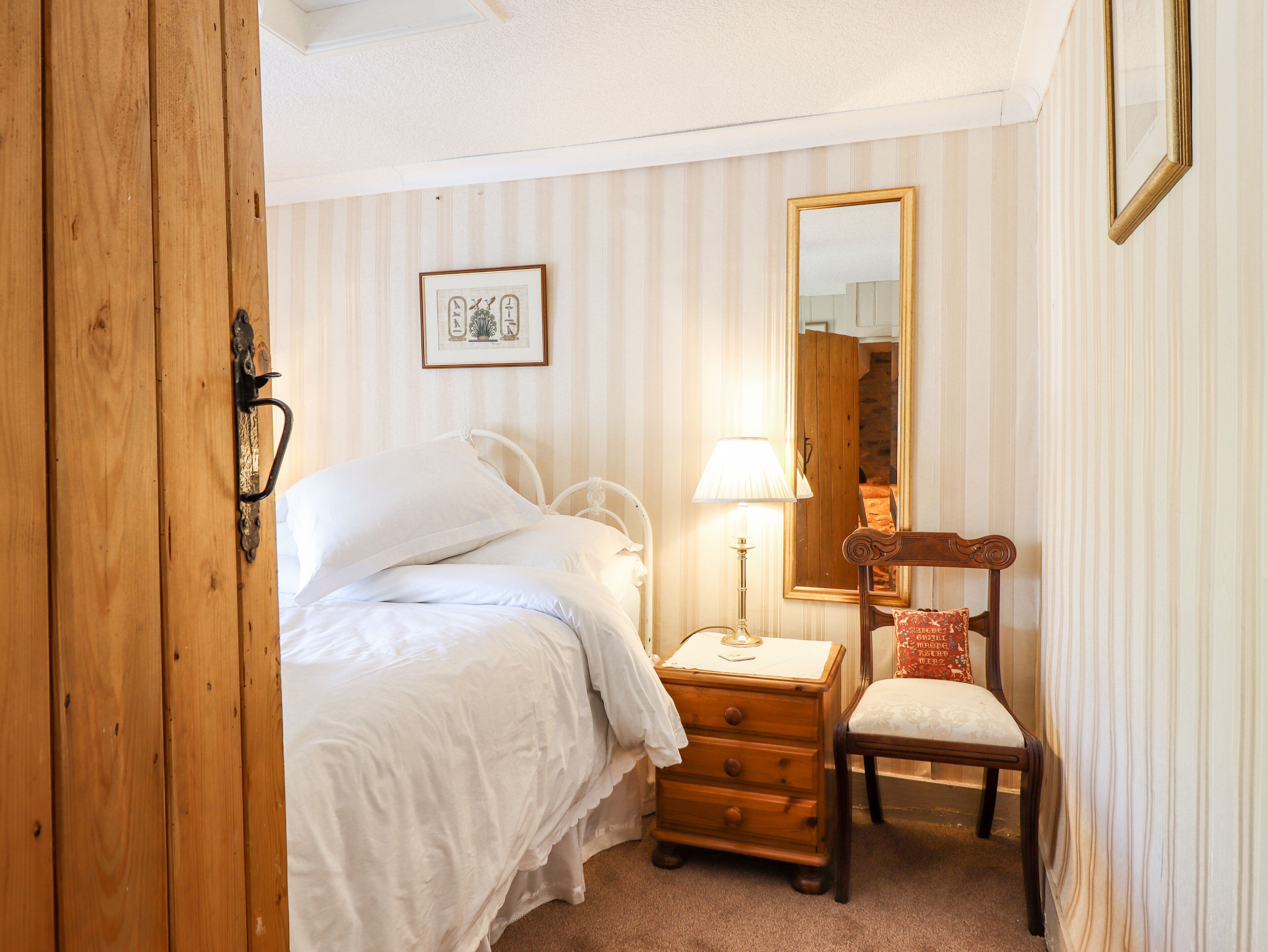 A bedroom with a bed, a wooden dresser, a chair, a lamp, and a mirror.
