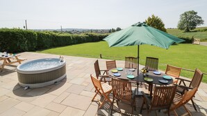A patio with a hot tub, wooden chairs, a table set for dining, and a green umbrella. - Lea Farm House (Kidderminster)