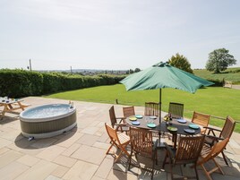 Un patio con un jacuzzi, sillas de madera, una mesa lista para comer y un paraguas verde.