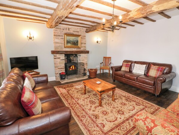 A cozy living room with a stone fireplace, leather sofas, a wooden coffee table, and a television.
