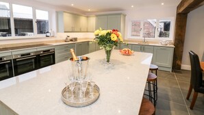A modern kitchen with a large island, built-in appliances, and a dining area with bar stools. - Lea Farm House (Kidderminster)
