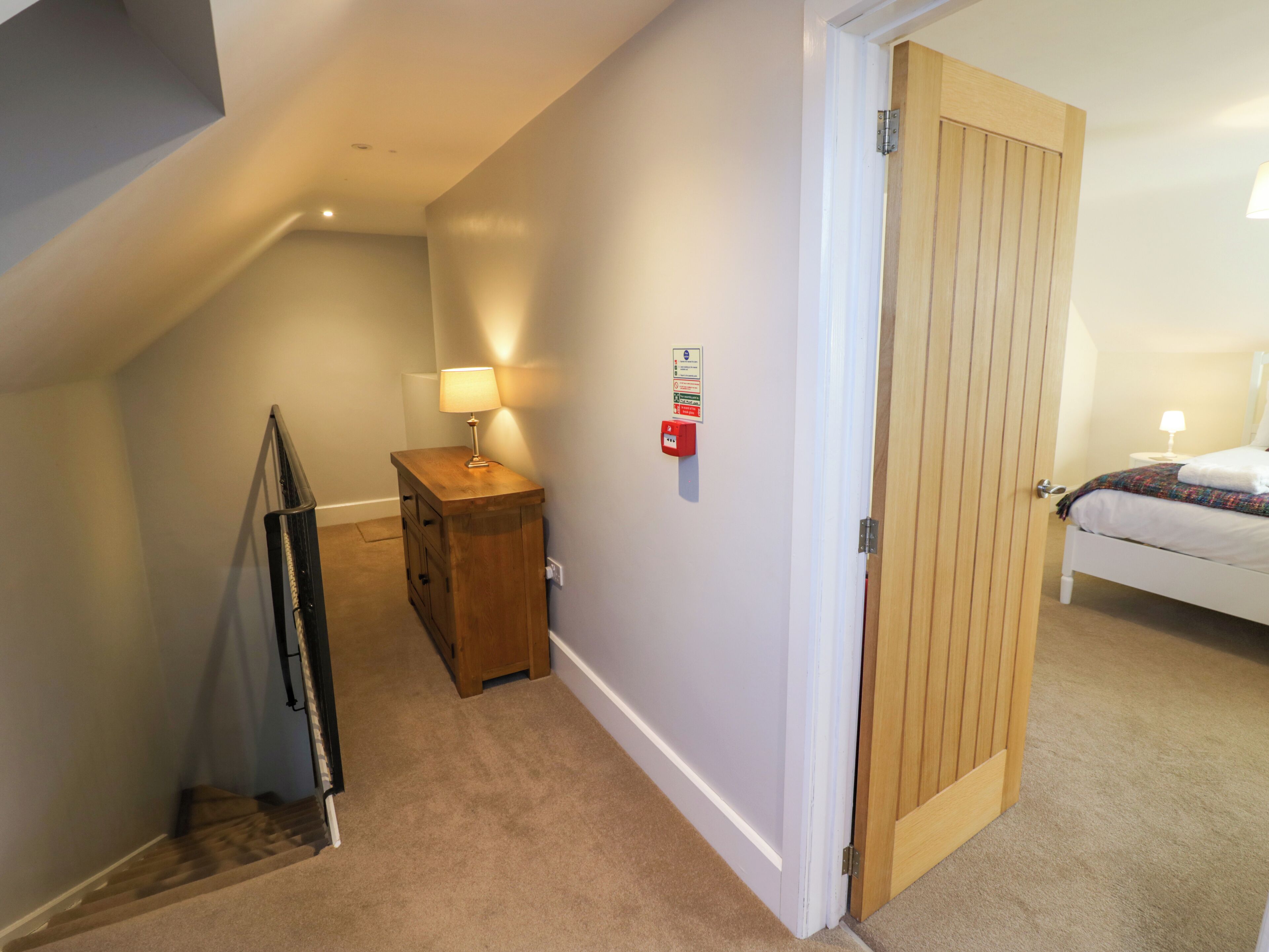 Een gang met een houten kast, een lamp en een deur naar een slaapkamer met een bed.