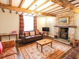 Una sala de estar acogedora con chimenea, vigas de madera, un sofá de cuero y un televisor.