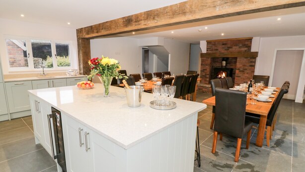 A modern kitchen with a large island, dining area with chairs, and a fireplace. - Lea Farm House (Kidderminster)