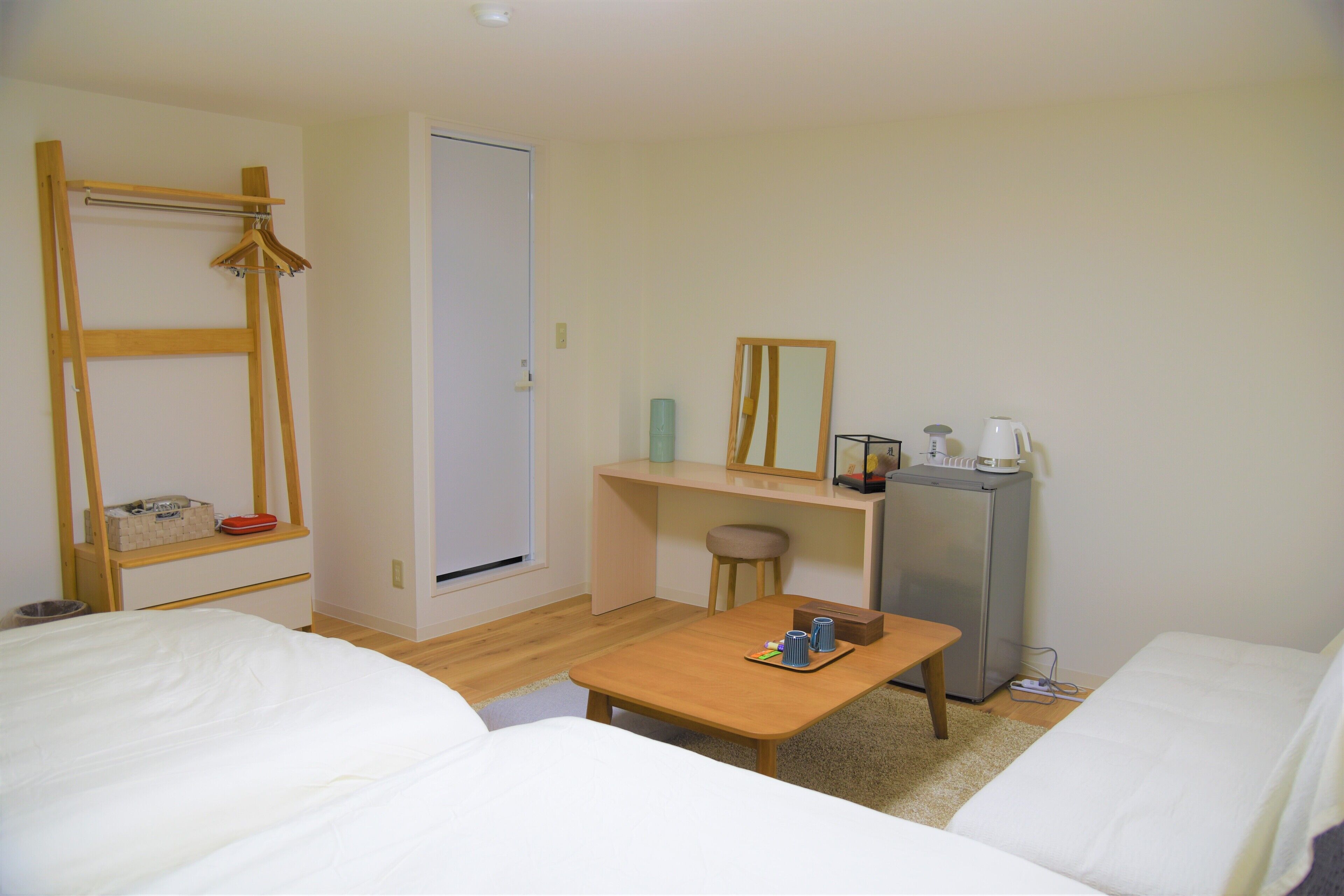 Habitación de hotel compacta con cama, un escritorio pequeño, una silla, una mesa con una bandeja de objetos, un espejo y un refrigerador.