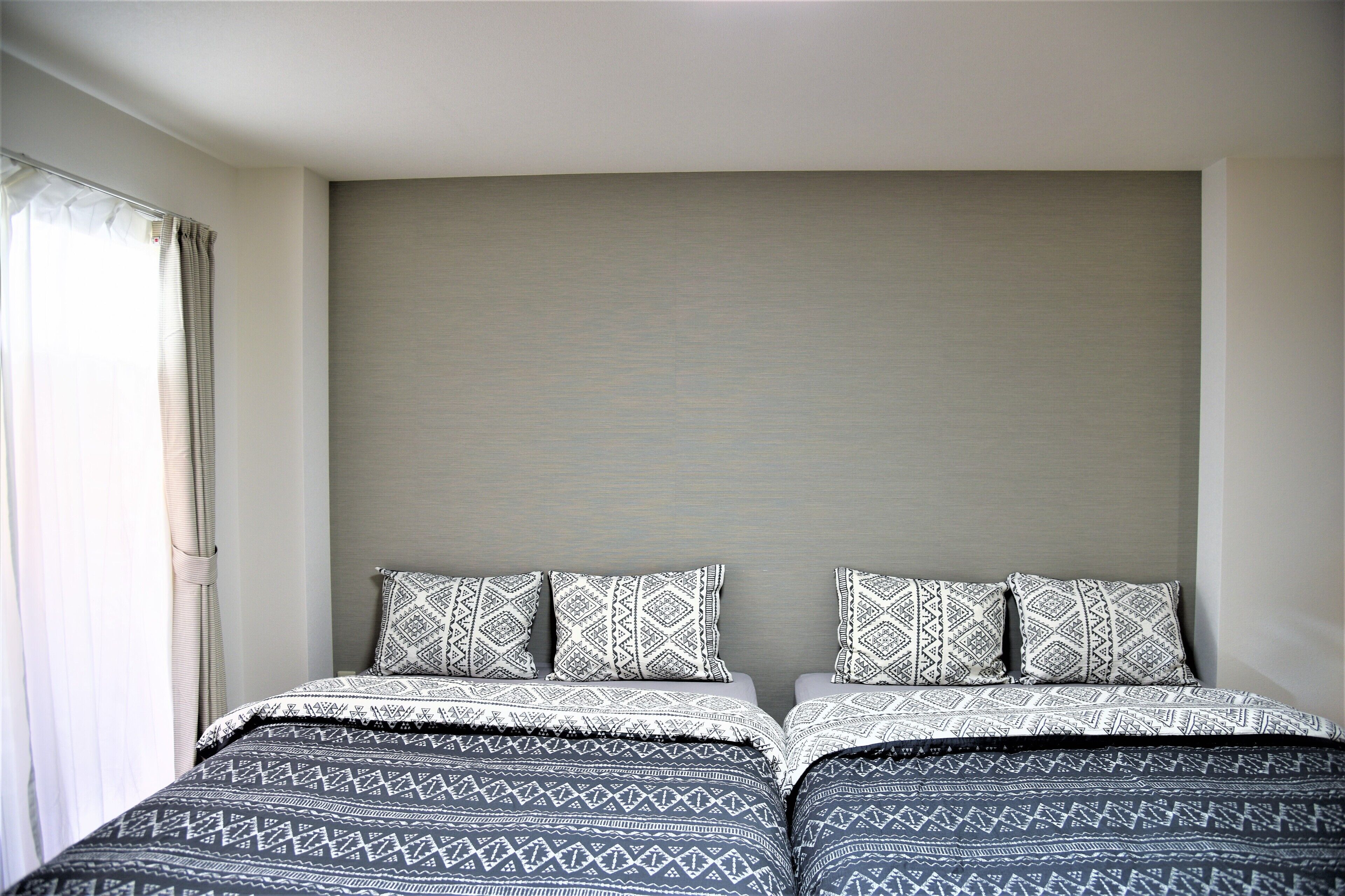 A bedroom with two beds, each with patterned bedding and pillows, a neutral-colored headboard, and a window with curtains.