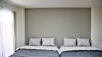 A bedroom with two beds, each with patterned bedding and pillows, a neutral-colored headboard, and a window with curtains.