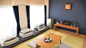 A modern living room with a sofa, a wooden table, tatami mats, and a small refrigerator. - U-Shuku Fushimi Inari (Kyoto)