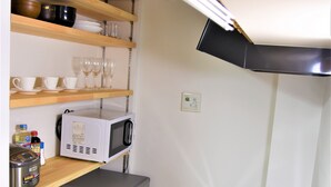 A compact kitchen with a microwave, refrigerator, and sink. There are shelves with cups and glasses, and a small cabinet with bottles. - U-Shuku Fushimi Inari (Kyoto)