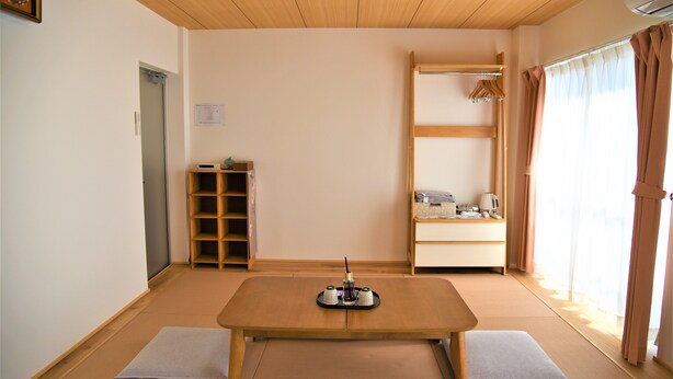 A room with tatami flooring, a low wooden table, a shelf with items, a wardrobe, and a window with curtains. - U-Shuku Fushimi Inari (Kyoto)
