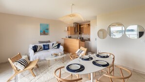 A compact living space with a dining area, kitchenette, and a sofa with cushions. - HEOL - appartement 2 chambres - vue mer et parking (Dinard)