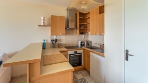 A compact kitchen with wooden cabinets, a built-in oven, a dishwasher, and a hanging light fixture. - HEOL - appartement 2 chambres - vue mer et parking (Dinard)