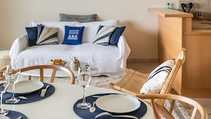 A modern living room with a dining area, featuring a sofa, dining table, chairs, and a kitchen area with wooden cabinets. - HEOL - appartement 2 chambres - vue mer et parking (Dinard)