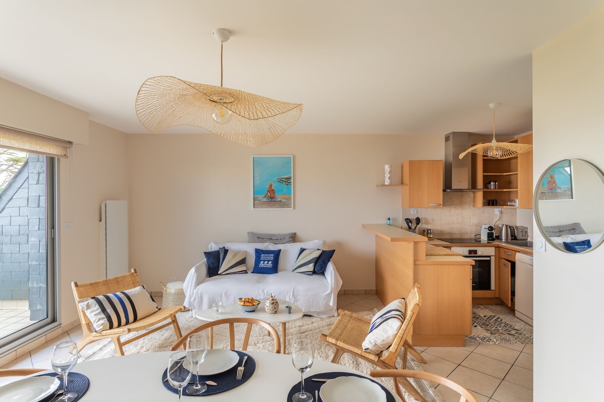 Una habitación de hotel compacta con una cama, una zona de comedor con una mesa dispuesta para dos personas, una kitchenette y un ventanal grande.