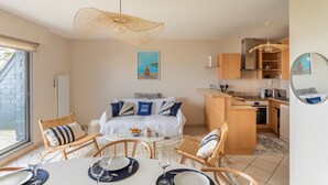 A compact hotel room with a bed, a dining area with a table set for two, a kitchenette, and a large window. - HEOL - appartement 2 chambres - vue mer et parking (Dinard)