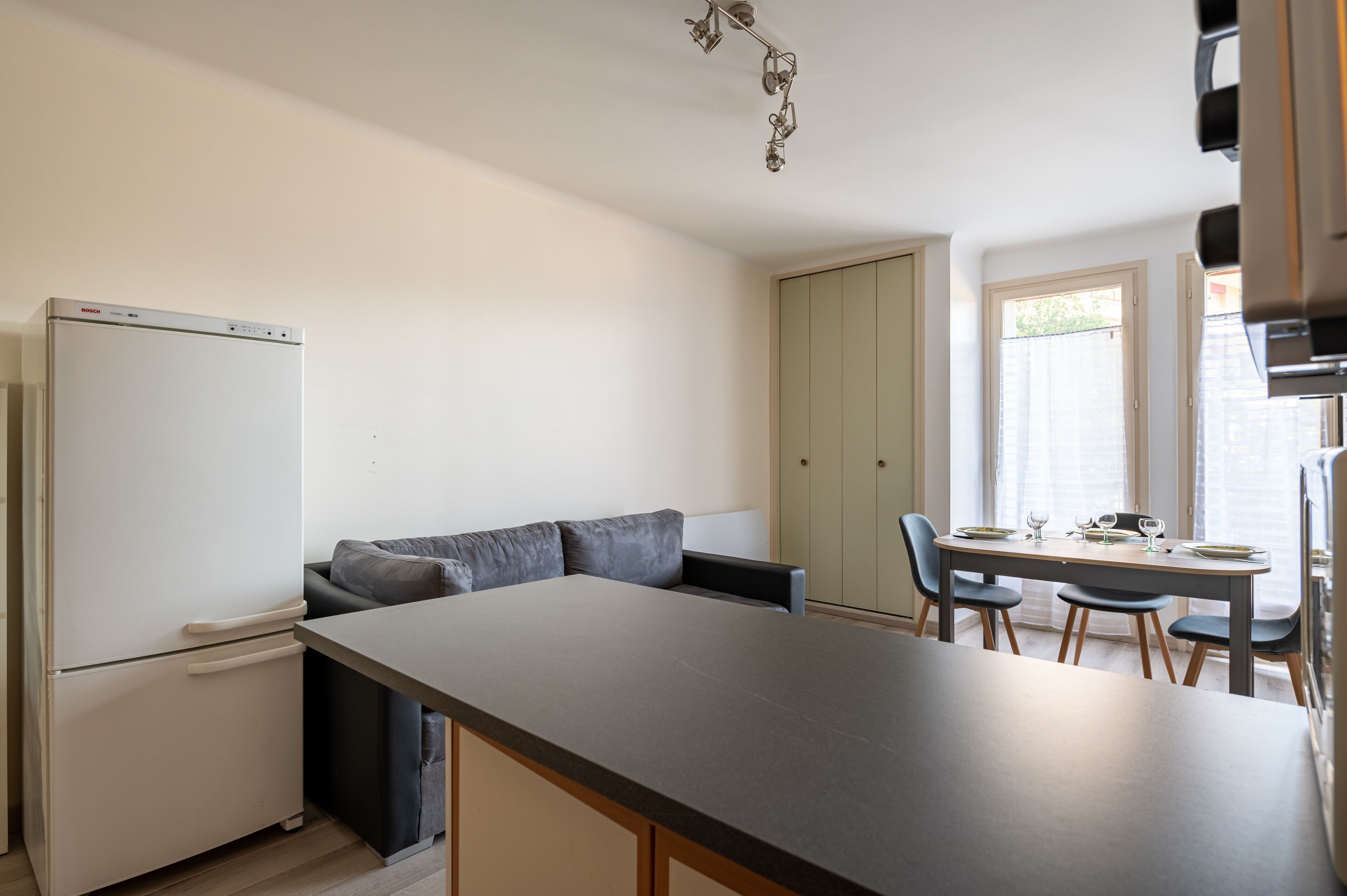 A compact kitchen with a refrigerator, a dining table with chairs, and a built-in bench.