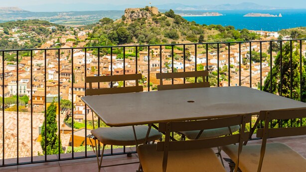 A balcony with a table and chairs overlooking a coastal town with a prominent hill and a ship in the distance. - Apartment near the center with wonderful views of Begur. (Begur)