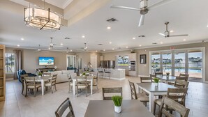 A spacious kitchen with modern appliances, a dining area with wooden tables and chairs, and a large window overlooking a pool. - BEAUTIFUL 3BD 2.5BA TOWNHOME, POOL, GYM  by BHOF (Naples)