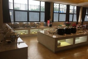 A hotel dining area with a central island, seating arrangements, and large windows providing natural light.