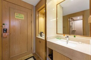 A hotel bathroom with a wooden door, a sink with a mirror, and a shower visible through the glass door. - Vienna Hotel (Ganzhou Railway Station Wanda Plaza Branch) (Ganzhou)