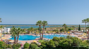Ein Poolbereich mit mehreren Pools, Palmen und Blick auf das Meer.