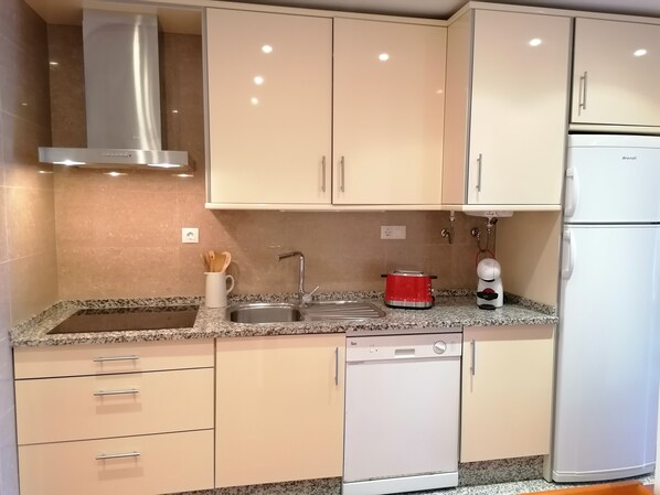 A kitchen with a stainless steel range hood, a sink with a faucet, a red toaster, a coffee maker, and a white dishwasher. - Casa da Ria - Beautiful view to the sea and Ria Formosa in Algarve (Tavira)