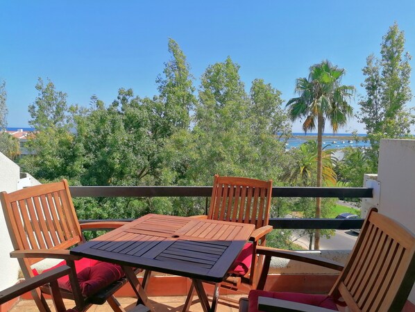 Ein Balkon mit Holztisch und -stühlen, der einen malerischen Blick auf das Meer und üppige Vegetation bietet.