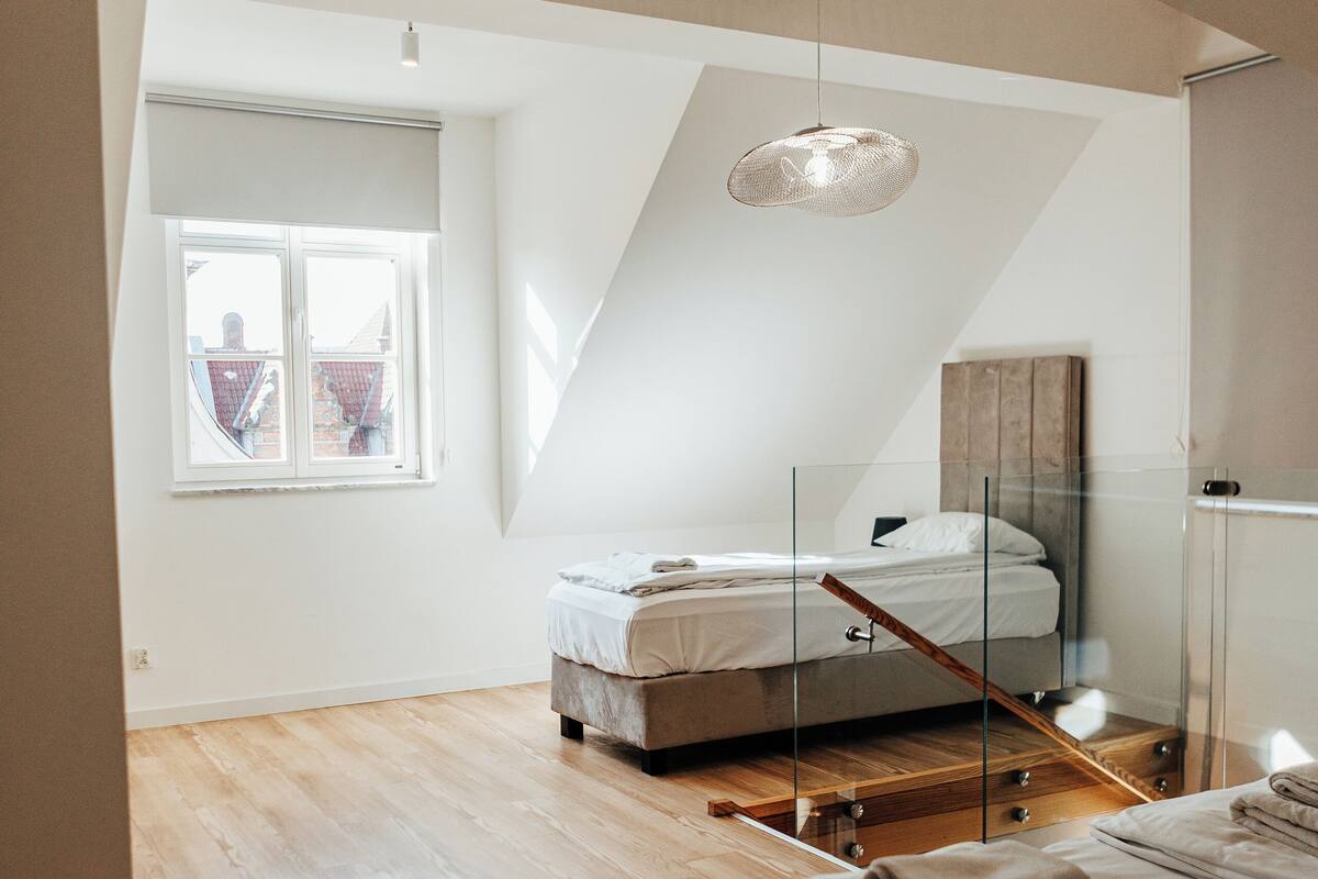 A bedroom with a large bed, a smaller bed, a window, and a hanging light fixture.