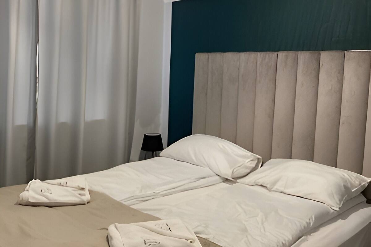 A hotel room with a bed, a bedside table, a lamp, and a hanging light fixture.