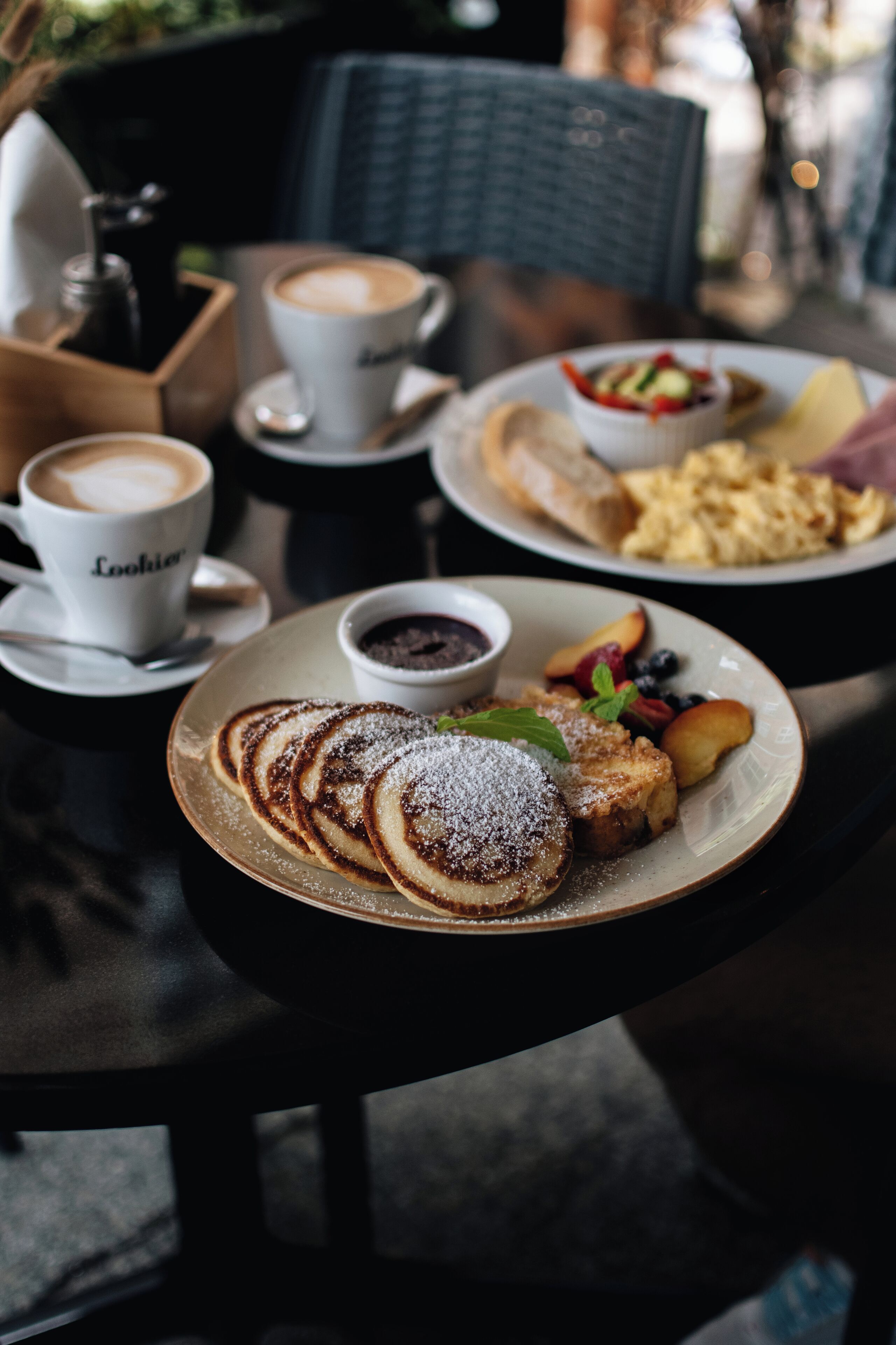 A dining table with a plate of pancakes, a cup of coffee, and a bowl of fruit.