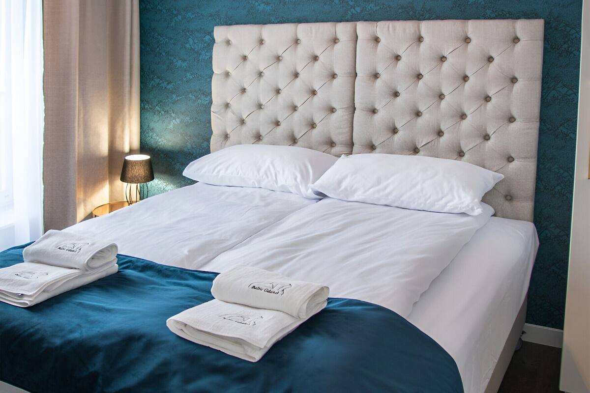 A neatly made bed with white linens and blue accents, a tufted headboard, and a hanging light fixture.