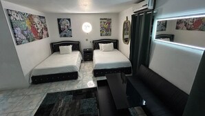 Una habitación pequeña y bien iluminada con dos camas, un sofá, una mesa de café y obras de arte en las paredes.