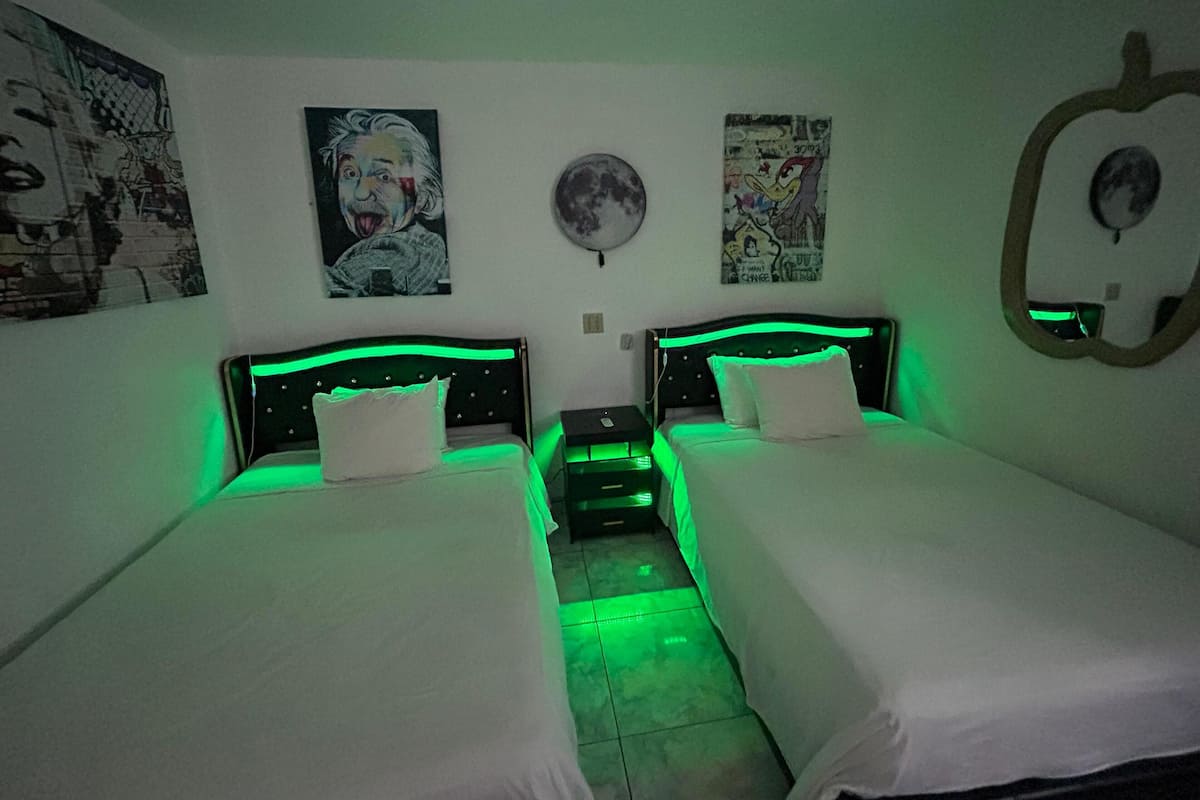 A twin room with two beds, green under-bed lighting, and various posters on the walls.