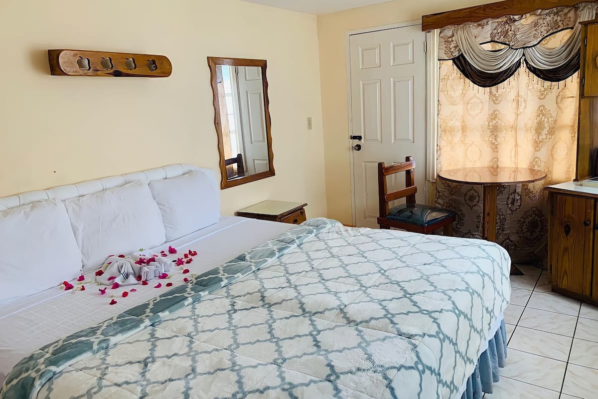 A bedroom with a bed, a chair, a desk, a mirror, and a door.