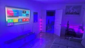 Una sala de estar moderna con un televisor de pantalla plana montado en la pared, un sofá y un escritorio con una silla.