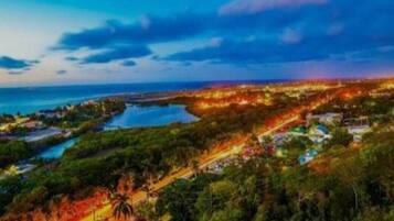 A coastal landscape with a view of the sea, a river, and a town with illuminated buildings.
