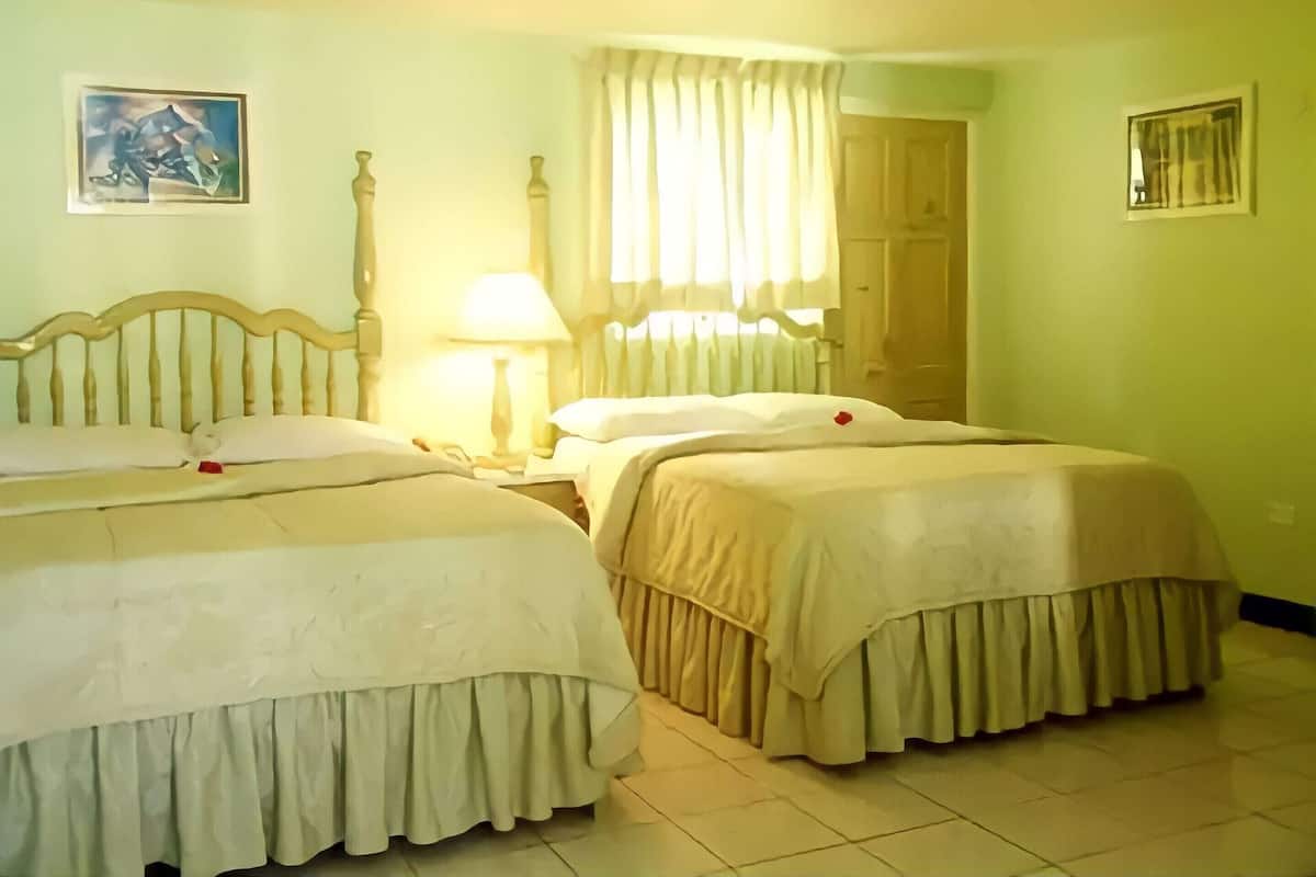 A hotel room with two beds, a nightstand, a lamp, a window with curtains, and a door.