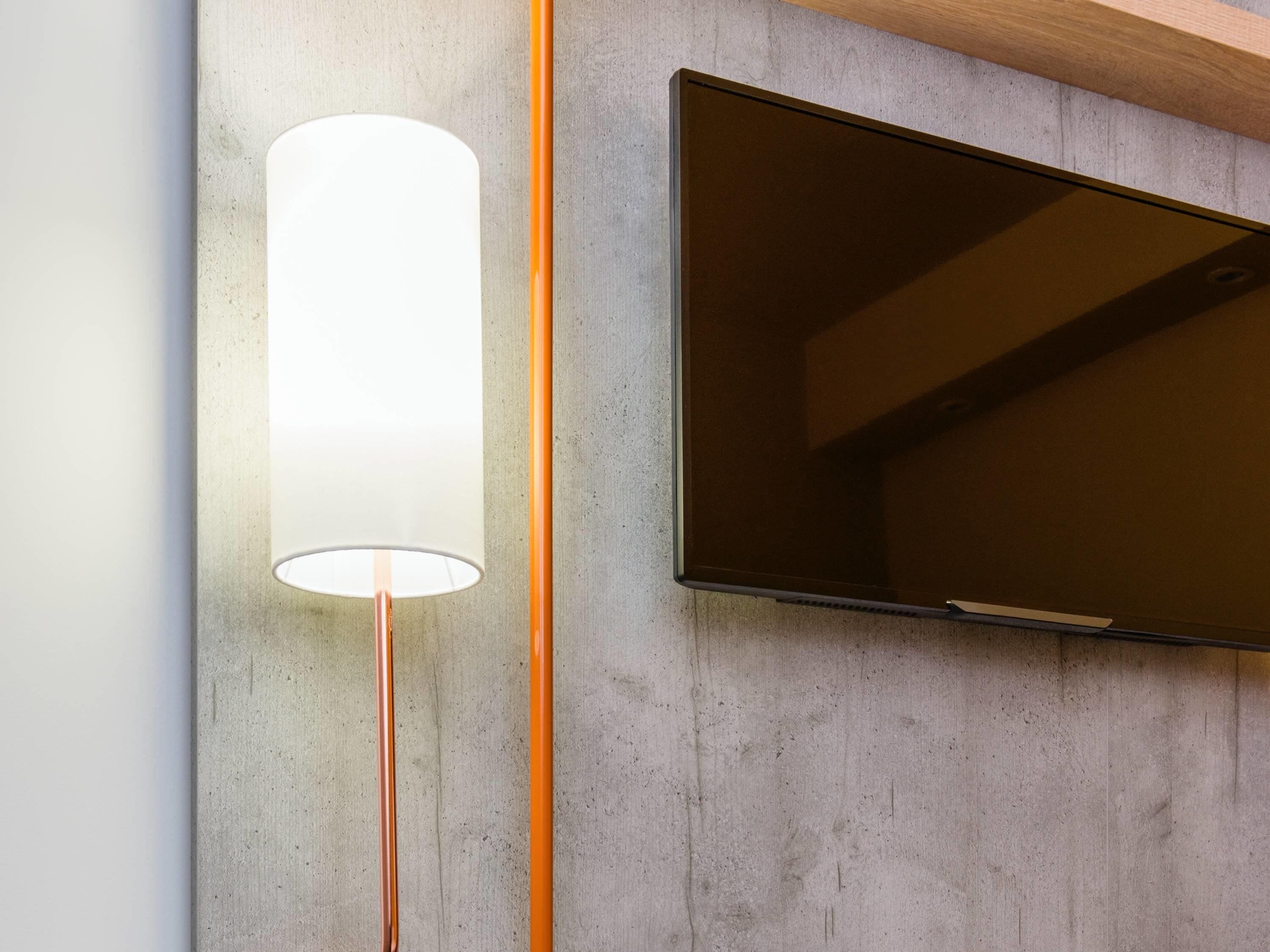 En platt-TV monterad på en vägg av betong, med en cylindrisk lampa placerad bredvid.