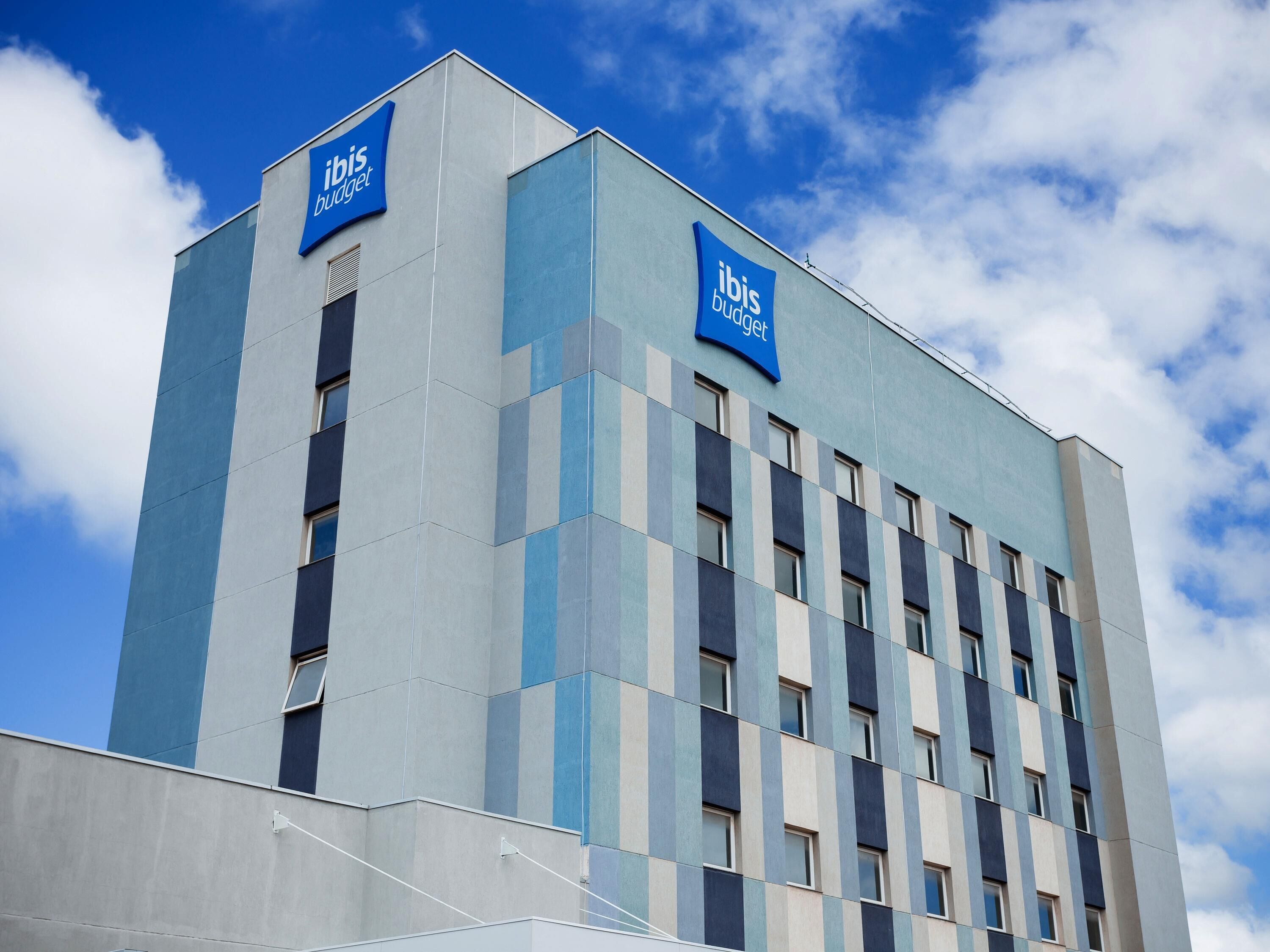 A modern building with 'ibis budget' signage, featuring a geometric facade and multiple windows.