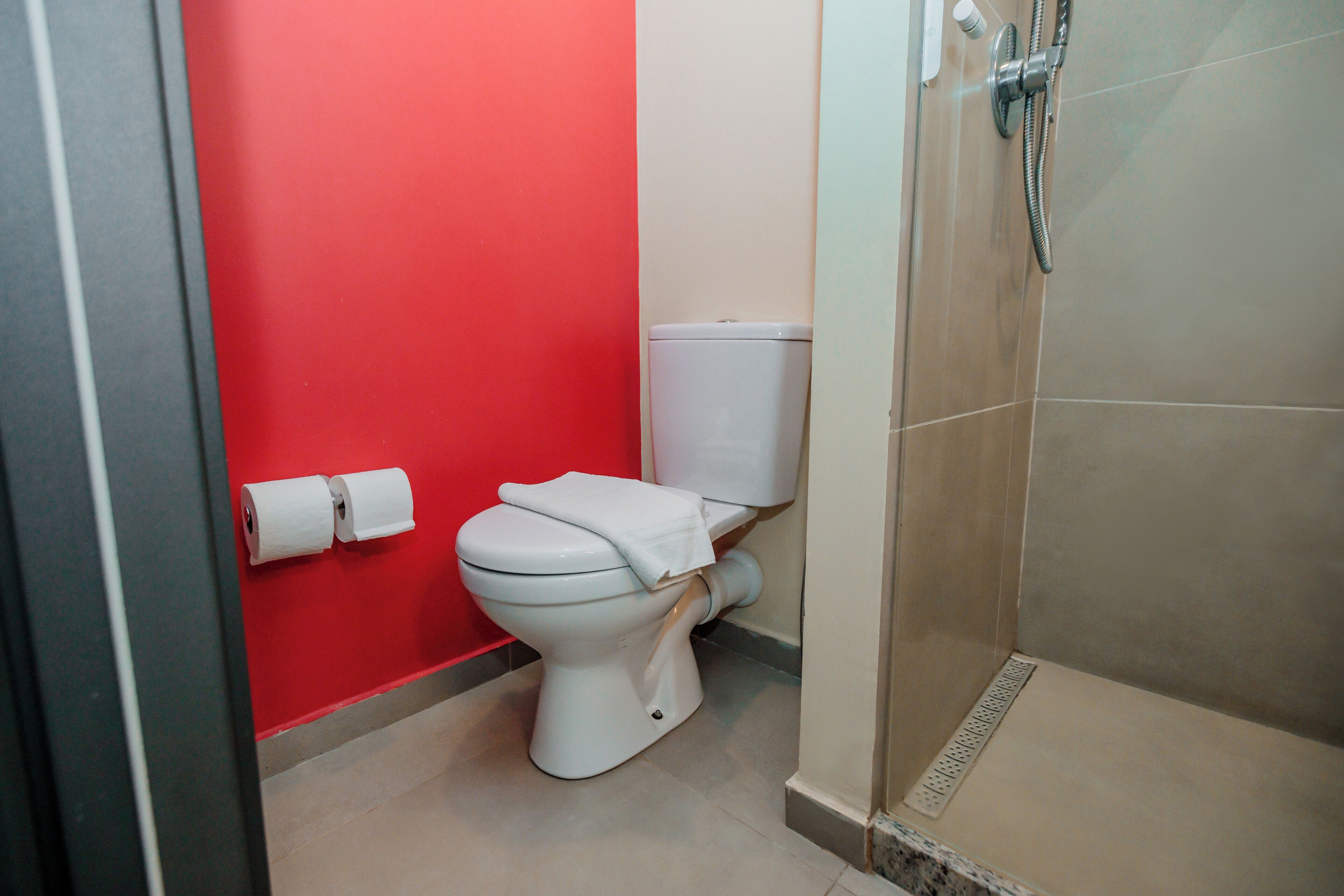 A bathroom with a red wall, a white toilet, and a shower area.