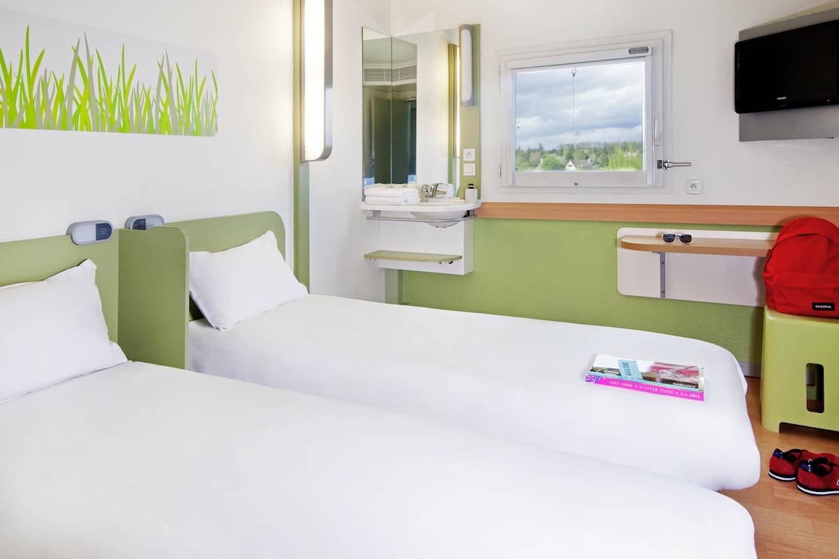 A hotel room with two beds, a bathroom, a TV, and a window with a view.