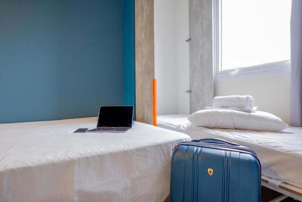 Ein Hotelzimmer mit einem Bett, einem Laptop auf dem Bett und einem blauen Koffer.