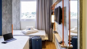 A hotel room with a bed, a desk with a laptop, a suitcase, a TV mounted on the wall, and a window with curtains. - Ibis Budget Capao Bonito (Capao Bonito)