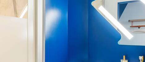 Un baño con pared azul, lavamanos blanco, espejo y toalla.
