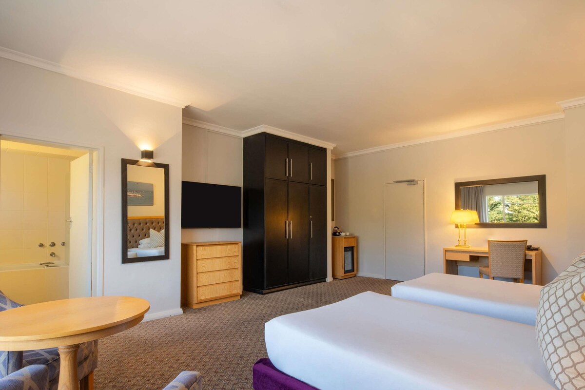 A hotel room with a bed, a desk with a chair, a TV, a wardrobe, and a small table.