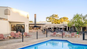 A pool area with lounge chairs and umbrellas, a building with a chimney, and outdoor seating.