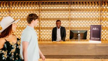 A reception desk with a geometric patterned wall, a HP monitor, and a 'Priority Welcome' sign.