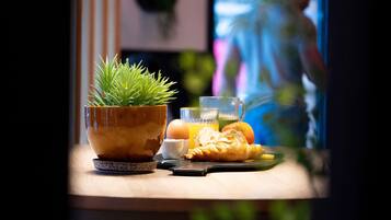 Un desayuno con una planta en maceta, un croissant, un vaso de jugo de naranja y un cuenco de huevos sobre una mesa de madera.