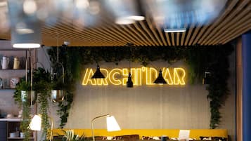 A restaurant interior with a neon sign, seating, pendant lighting, and greenery.