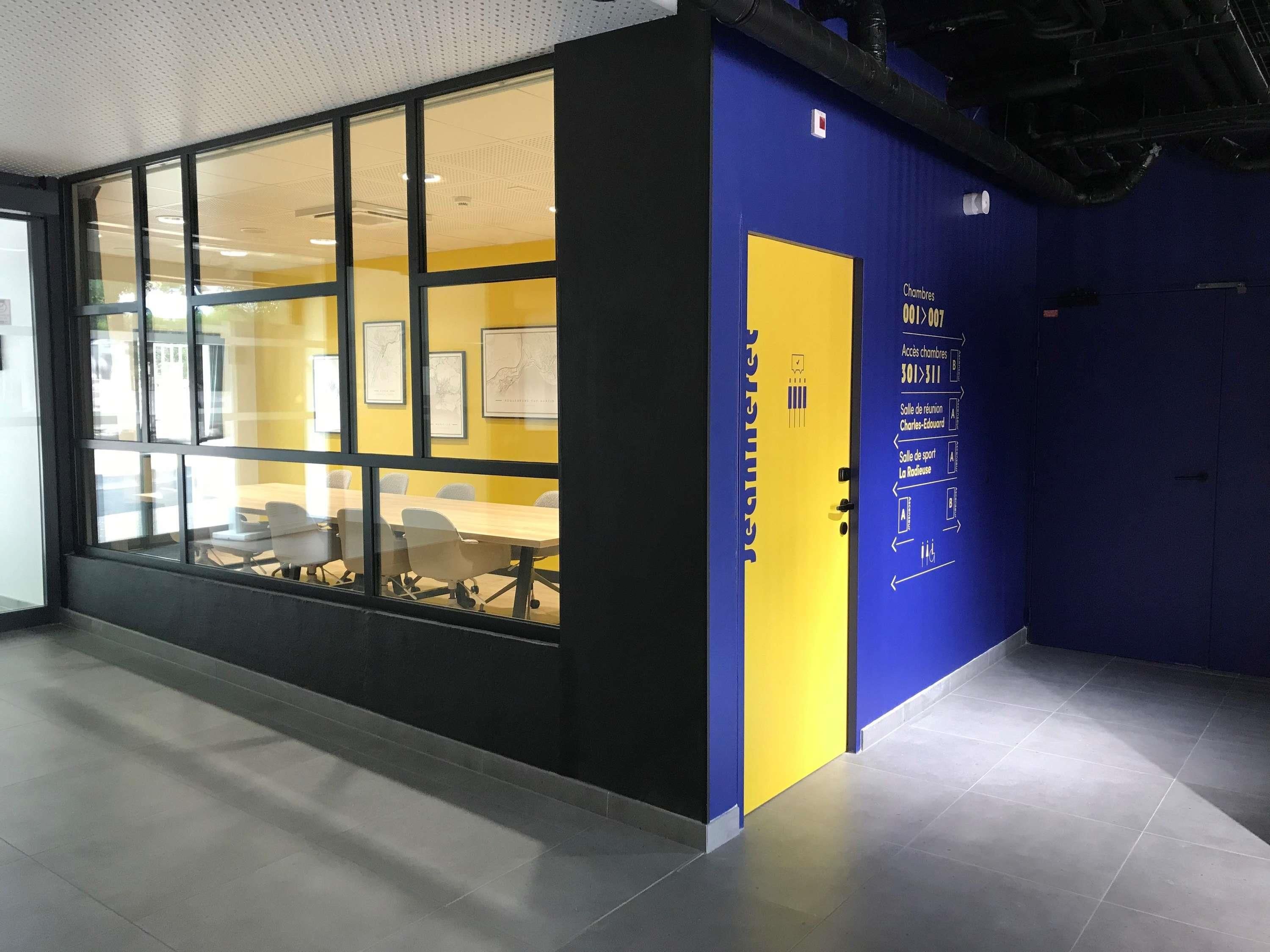 Un espace de bureau moderne doté de grandes fenêtres, d’une table de réunion et d’une décoration aux couleurs bleu et jaune.